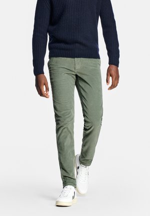 Grüne Cordhosen mit figurbetontem Schnitt, kombiniert mit einem marineblauen Strickpullover und weißen Turnschuhen. Strukturierter Stoff mit vertikalen Streifen.