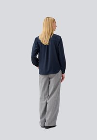 Maglietta a maniche lunghe blu navy dallo stile morbido, abbinata a pantaloni grigi larghi realizzati in tessuto testurizzato. La parte superiore è semplice e priva di fantasie.