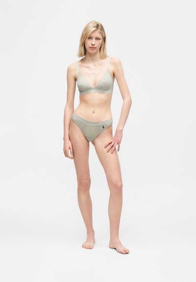 Νεαρή γυναίκα στέκεται ξυπόλυτη φορώντας ανοιχτό γκρι μπραλέτα και αντίστοιχα σλιπ με το λογότυπο Polo Ralph Lauren σε ένα απλό λευκό φόντο.