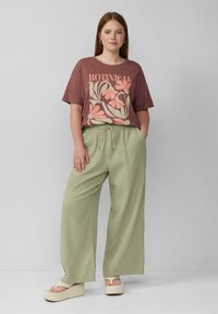 Roestkleurig t-shirt met bloemgraphic; losse, lichtgroene textuurpants; beige platform sandalen; minimale accessoires.