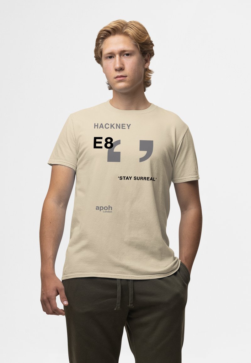 Béžové bavlněné tričko s černým a šedým textem: "Hackney," "E8," a "'STAY SURREAL'" s uvozovkami a logem dole.