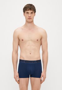 Boxer briefs bleu marine avec une ceinture élastique noire arborant le nom de la marque "DIESEL" en lettres majuscules. Texture de tissu lisse.