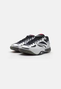 Chaussures de sport argent et noires avec un dessus texturé, un design épuré et une semelle épaisse avec une adhérence en caoutchouc et des détails de coussinage à air.