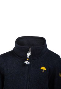 Chaqueta de punto azul oscuro con un cuello alto, cremallera central con tira para tirar y un pequeño logo de paraguas amarillo en el pecho.