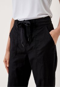 Pantalons noirs amples avec une surface texturée, poches avant et une taille élastique dotée d'un cordon de serrage réglable.
