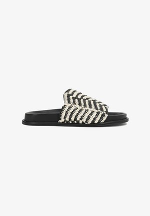 Sort slidesandal med flettet sort-og-hvidt chevronrem og glat flad sål, set fra siden på hvid baggrund.