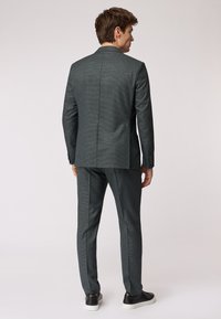 Completo grigio scuro con un sottile motivo a quadri, dotato di uno spacco singolo, vestibilità sartoriale e abbinato a sneaker nere.