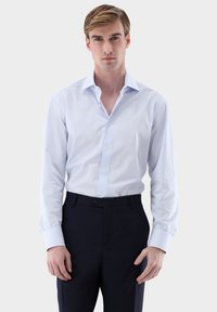 Hellblau-weiß gestreiftes Hemd mit Kragen, langen Ärmeln und durchgehender Knopfleiste. Kombiniert mit dunkelblauen Hosen. Glatte Textur.