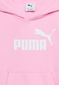 Ροζ φούτερ με κουκούλα με λευκό λογότυπο Puma και κείμενο στο στήθος, που δείχνει την ετικέτα μεγέθους μέσα στον γιακά.