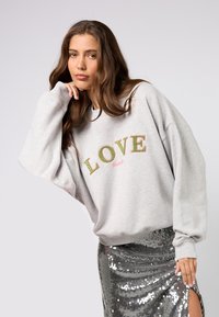 Világosszürke pulóver vastag zöld �és rózsaszín "LOVE" felirattal. Puha anyagból készült, bő, túlméretezett szabással és széles ujjakkal.