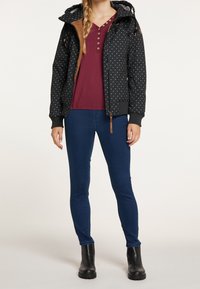 Černá zateplená bunda s bílými puntíky, hnědé kožené akcenty, zipové uzavření, v kombinaci s vínovým topem a modrými džíny, nošená s černými botami.