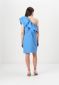 Robes bleu à une épaule avec un accent froncé. Tissu lisse avec une silhouette ajustée, se terminant au milieu de la cuisse. Jambes et talons de la personne visibles.