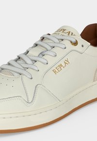 Λευκό δερμάτινο αθλητικό παπούτσι με μπεζ λεπτομέρειες, λευκά κορδόνια, χρυσό λογότυπο "REPLAY" στο πλάι και ανοιχτοκαφέ λαστιχένια σόλα.