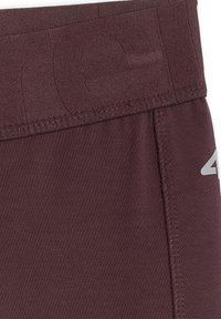 Gros plan d’un tissu bordeaux avec une ceinture élastique et des coutures visibles, avec un logo "4F" partiellement réfléchissant sur le côté droit.