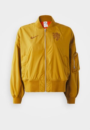 Dzeltena bumbas jakas ar elastīgiem aprocēm un apakšmalu, ar priekšējo rāvējslēdzēju, sānu kabatām un logotipa detaļu uz krūtīm.