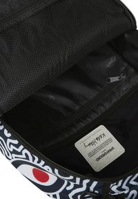 Interior de mochila negra con bolsillo de malla, textura suave y patrón abstracto blanco. Cuenta con una etiqueta y un tirador de cremallera para un cierre seguro.