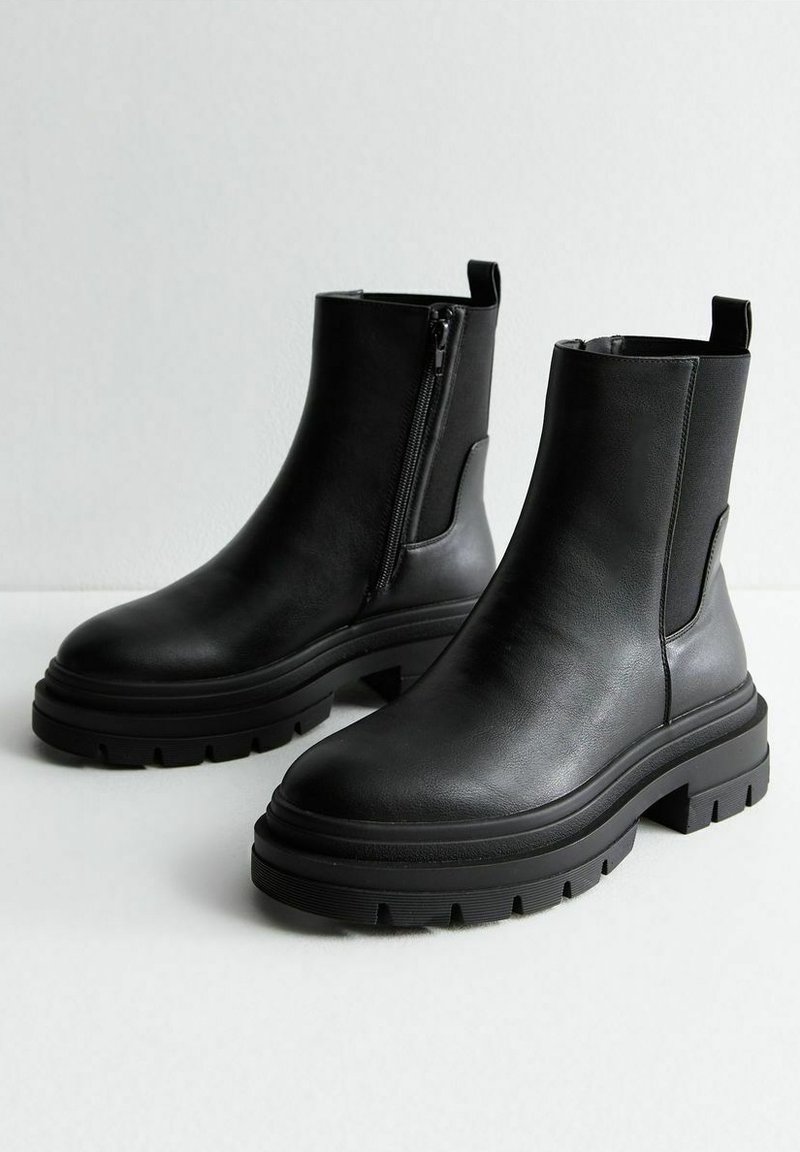 Bottines en cuir noir avec une semelle épaisse, zip latéral et ancre. Texture lisse et design minimal, adaptées à diverses occasions.