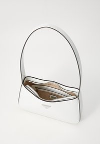 Sac à main en cuir blanc, de forme arrondie, avec une fermeture éclair, des garnitures marron et une poche intérieure. Équipé d'une seule sangle d'épaule courbée.
