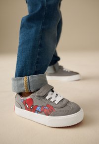 Baskets en toile grise avec un motif Spider-Man, lacets blancs et semelle en caoutchouc. Jean avec revers retroussés présentant des accents bleus et dorés.