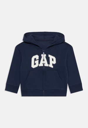 Marineblå lynlåshættejakke med forlommer og hvide "GAP"-bogstaver på brystet, med lange ærmer og hætte.