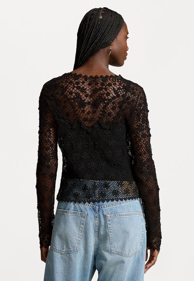 Black lace long-sleeve top featuring intricate floral patterns with a scalloped hem, paired with light blue denim jeans.