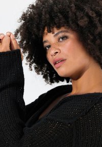 Cardigan nero in maglia con un design morbido e strutturato. Presenta maniche ampie e una scollatura profonda che esalta il motivo della maglia.