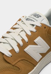 Κοντινό πλάνο καφέ και μπεζ αθλητικού παπουτσιού New Balance 498 με λευκά κορδόνια και μεγάλο λευκό λογότυπο "N" στην πλευρά.