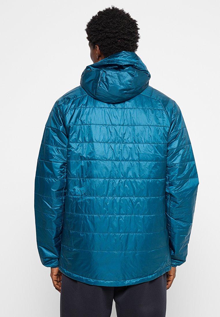 Chaqueta acolchada en tono verde azulado con capucha, diseño acolchado y textura suave. La parte trasera es lisa y tiene un dobladillo ligeramente redondeado.