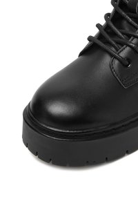 Čierna kožená členková obuv s okrúhlou špičkou, hrubou platformou a šnurovaním. Hladký povrch s minimálnym prešívaním.