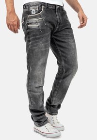 Jeans in denim grigio con una vestibilità slim, dotati di molteplici tasche e cuciture in contrasto. Abbinati a sneakers bianche.