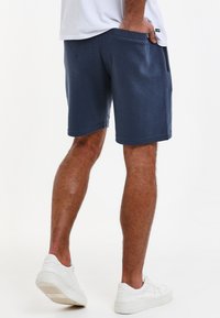 Námořnické modré šortky z texturované látky s bočními kapsami a uvolněným střihem. Nosí se s bílými teniskami, což vytváří ležérní styl.