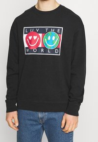 Felpa nera con grafica frontale che mostra faccine sorridenti rosse e verdi e il testo "AMA IL MONDO." Design classico con collo a giro, tessuto morbido.