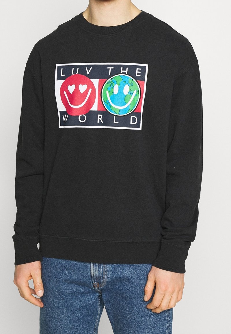 Felpa nera con grafica frontale che mostra faccine sorridenti rosse e verdi e il testo "AMA IL MONDO." Design classico con collo a giro, tessuto morbido.