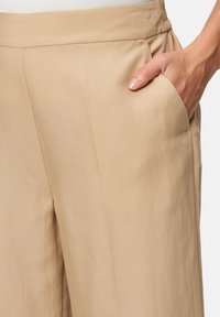 Beige linen pants featuring a smooth texture, side pocket, and elastic waistband for comfort, showcasing minimalist design and tailored fit.