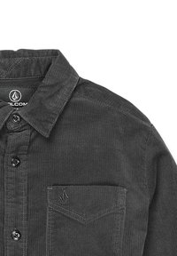 Camisa de pana gris con cuello extendido, tapeta de botones y un bolsillo en el pecho. Presenta una tela texturizada y una etiqueta con el logo en el interior del cuello.
