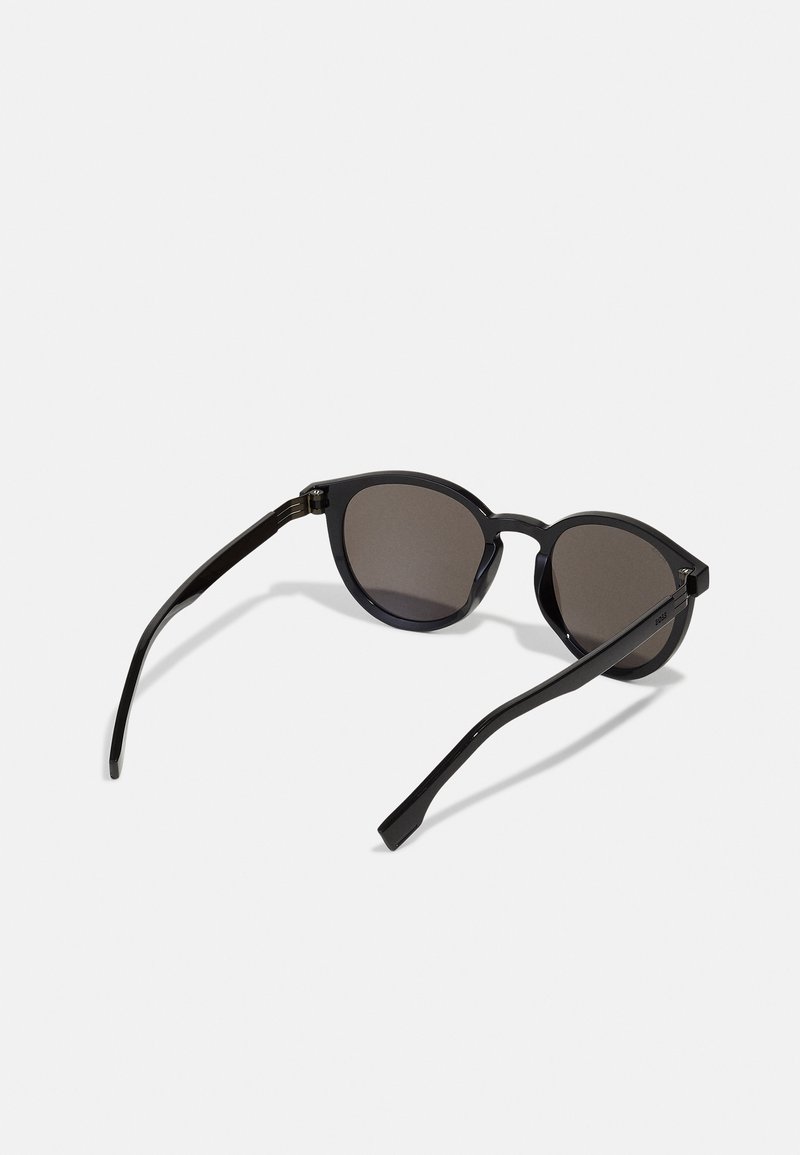 Occhiali da sole neri con lenti rotonde, montatura in plastica elegante e bracci sottili. Le lenti presentano una tonalità scura, che offre protezione dai raggi UV.
