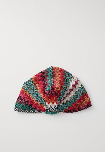 Căciulă tricotată cu un model în zigzag în culori vibrante: roșu, turquoise, negru și alb. Material texturat cu un detaliu de nod în vârf.