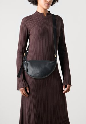 Czarna skórzana torba na ramię o zaokrąglonym kształcie i teksturowanej fakturze, wyposażona w złocisty zatrzask i regulowany pasek, na sukience z prążkowanej tkaniny.