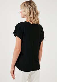 Zwarte T-shirt met korte mouwen, een losse pasvorm, ronde halslijn en naaddetails aan de achterkant. Zachte stof met een gladde textuur.