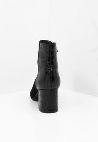 Botín negro hasta el tobillo con un diseño de cuero texturizado con estampado de cocodrilo, adornos de ante mate y un tacón grueso. Cierre con cremallera en la parte posterior visible.