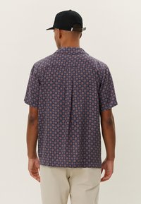 Short-sleeve shirt in navy blue with a circular pattern in red and white, made from lightweight fabric, featuring a straight cut and collar.