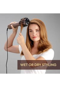 Vrouw met schouderlang rood haar die haar stylet met een elektrische hete luchtborstel, tekst: "Nat of droog stylen" tegen een grijze achtergrond.