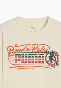T-shirt color crema con maniche corte, caratterizzato da un design grafico in verde, arancione e nero che include la scritta "Bend the Rules" e una figura che pattina.