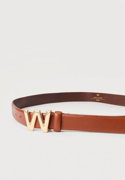 Καφέ δερμάτινη ζώνη με μεγάλο αγκράφα σε χρυσό τόνο σχήματος "W" και ραμμένες άκρες, τοποθετημένη επίπεδα σε ανοιχτόχρωμη επιφάνεια.