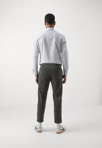 Langärmliges, hellblaues kariertes Hemd mit Button-Down-Kragen, kombiniert mit dunkelgrünen Cordhosen und weißen Sneakers mit schwarzen Akzenten.