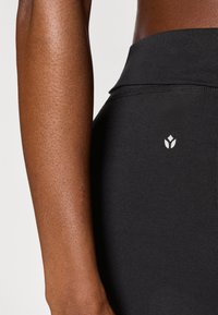 Μαύρο αθλητικό κολάν από ελαστικό υλικό, με ψηλή μέση και μικρό λευκό λογότυπο στην περιοχή του ισχίου. Λείο υφή.