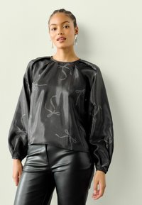 Juoda satino palaidinė su pūstomis rankovėmis, apvalios iškirptės ir sidabrinio kaspinų raštais. Derinama su prigludusiomis juodomis odinėmis kelnėmis.