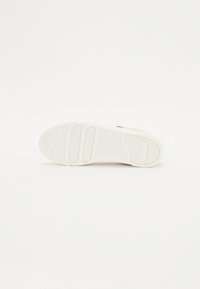 Suola di sneaker bianca con gomma testurizzata, dotata di scanalature per aderenza e una superficie liscia. Design semplice senza marchi visibili.