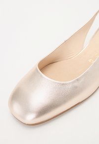Metallisk roséguldfärgad slingback-sko med rund tå och slät textur på ovandelen. Mjuk beige innersula synlig inuti, minimalistisk design.