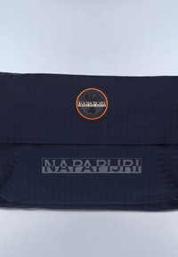 Marint blå axelväska med en strukturerad yta, med ett cirkulärt logopatch och namnet "NAPAPIJRI" i reflekterande bokstäver.